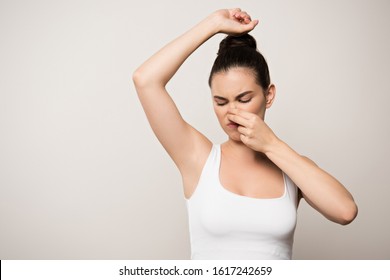 Displeased Woman Plugging Nose With Hand While Looking At Underarm Isolated On Grey