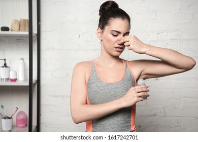 Displeased Woman Plugging Nose With Hand While Applying Deodorant On Underarm