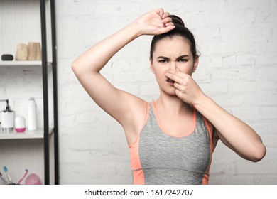 Displeased Woman Plugging Nose With Hand While Standing With Raised Hand And Looking At Camera