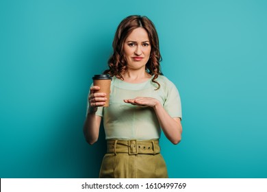 displeased woman showing refusal gesture while holding coffee to go on blue background