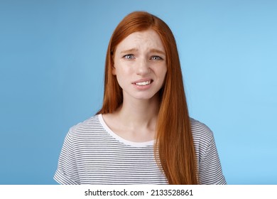 Displeased young awkward redhead girl cringe full disbelief smirking frowning confused look questioned doubtful hearing nuisance dumb story standing blue background uncertain