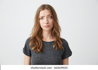 Displeased young beautiful girl looking at camera raising one eyebrow over white background.