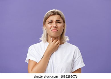 Displeased Young Stylish Caucasian Woman With Blond Hair And Tanned Skin Feeling Discomfort In Throat Having Inflammation Or Feeling Cold Touching Neck And Frowning Dissatisfied From Pain