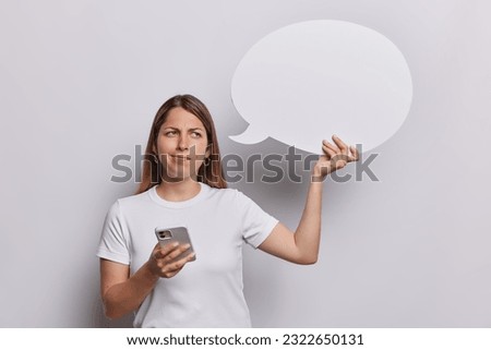 Displeased young woman in casual tshirt browses her smartphones email box while holding empty speech bubble eagerly awaiting your advert content showcasing your product or service wears t shirt