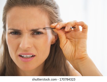 Displeased Young Woman Tweezing Eyebrows