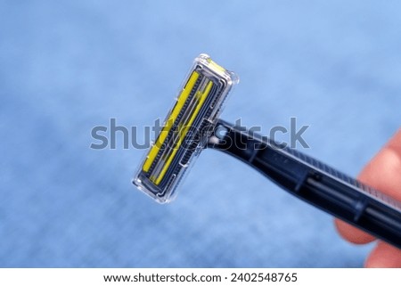 Disposable blue razor with steel sharp blades in hand on a jeans background. Hygiene accessories. Close up