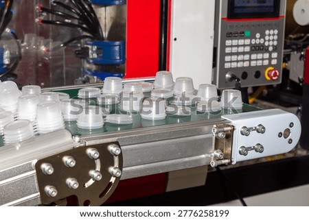 Disposable clear plastic containers on conveyor belt in factory. Industrial injection molding machine in background. Disposable tableware production process concept