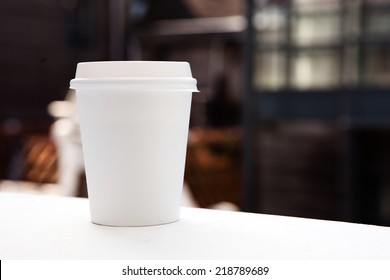 Disposable coffee cup on windowsill with blurred city in background. - Powered by Shutterstock