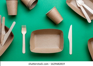 Disposable eco friendly food packaging. Brown kraft paper food containers on green background. Top view, flat lay. 