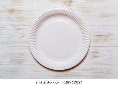Disposable eco paper plate on wood background. Eco-friendly, plastic-free tableware. Organic plate made of environmental material. Copy space. Top view. Flat lay