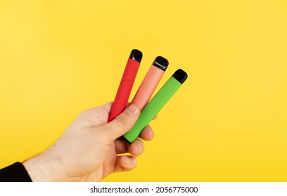 Disposable electronic cigarettes of different flavors in hand on a yellow background. The concept of modern smoking, vaping and nicotine.