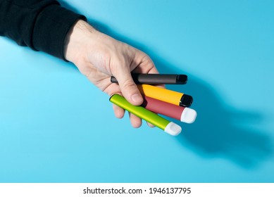 Disposable electronic cigarettes in hand closeup on a blue background with shadows. The concept of modern smoking, vaping and nicotine. Copy space