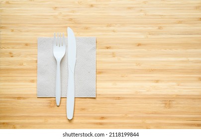 Disposable Fork And Knife On A Paper Napkin On A Wooden Background. Eco-friendly Cornstarch Cookware. View From Above. Copyspace.