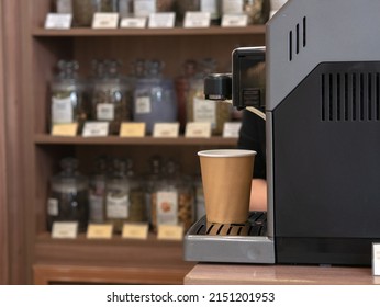 Disposable paper cup hot jet of milk with steam pouring from a coffee machine in a tea shop or coffee shop, background in blur.