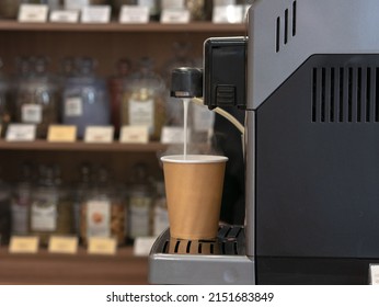 Disposable paper cup hot jet of milk with steam pouring from a coffee machine in a tea shop or coffee shop, background in blur.