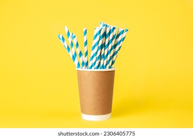 Disposable paper cup with striped paper straws on a yellow background.