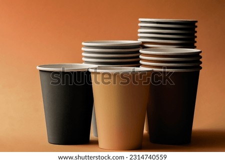 Disposable paper cups earth tone color on orange background. Glasses of different sizes and colors close up. Party utensils for different drinks.
