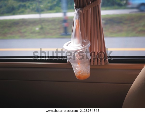 Disposable plastic glass of ice coffee hanging on\
curtain in the car.