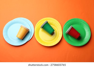 Disposable plastic tableware. Bright plates and cups on orange background, flat lay