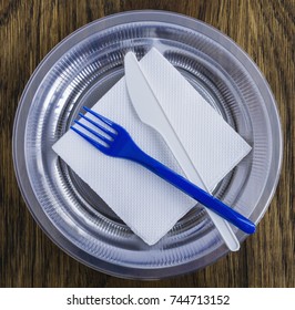 Disposable plastic tableware and paper napkins for picnics on wooden background.