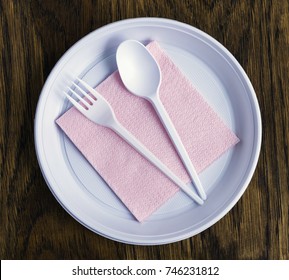 Disposable plastic tableware and pink paper napkins for picnics on wooden background.