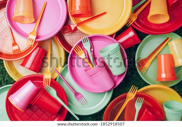 Disposable plastic tableware - plates, forks,\
spoons. Colored plastic disposable tableware on green grass moss\
background. Top view. Copy space. Birthday picnic utensil.\
Recycling plastic and\
ecology.