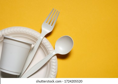 disposable plate, glass, spoon and fork of corn starch on a yellow background. biodegradable eco friendly picnic tableware. isolate. replacement of plastic with modern biomaterials. place for text