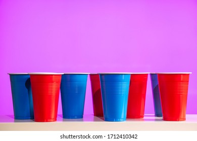 Disposable Red And Blue Plastic Party Beer Cups On A White Table Or Shelf With A Bright Modern Purple Background.