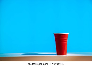 A Disposable Red Plastic Party Beer Cup On A White Table Or Shelf With A Bright Modern Blue Background.