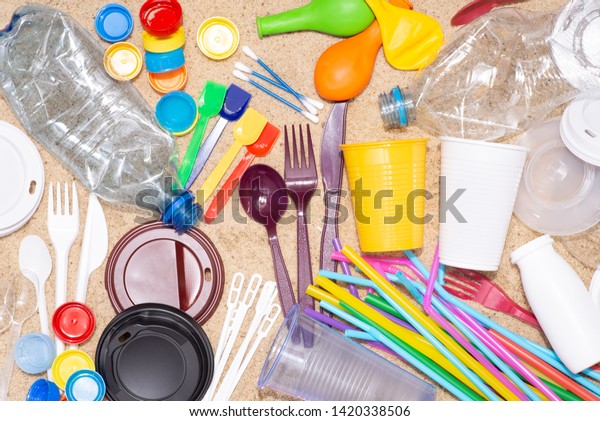 Disposable single use plastic\
objects such as bottles, cups, forks, spoons and drinking straws\
that cause pollution of the environment, especially oceans. Top\
view on sand