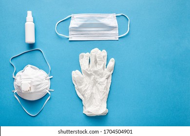 Disposable Surgical Mask, Reusable Medical Respirator, Latex Gloves And Alcohol Sanitizer Hand Spray For Cleaning Hygiene Protection Corona Virus Or Antibacterial, Shot On Blue Background, Top View.