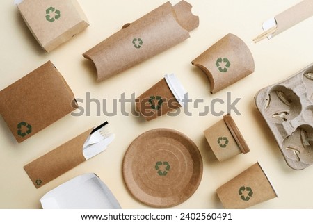 Disposable tableware made from biodegradable paper with recycling signs on a yellow background. View from above.