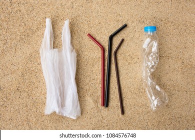 Disposable Water Bottle, Straws And Carrier Bag, Single Use Plastic Item, On Sandy Beach Background. Plastic Pollution Affecting Marine Ecology. Environment Concept. Top View.