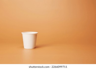 Disposable white single one recyclable cardboard paper cup isolated on the bright solid fond plain sandy beige background - Shutterstock ID 2266099711