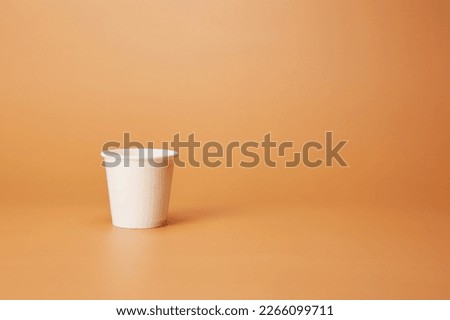 Disposable white single one recyclable cardboard paper cup isolated on the bright solid fond plain sandy beige background