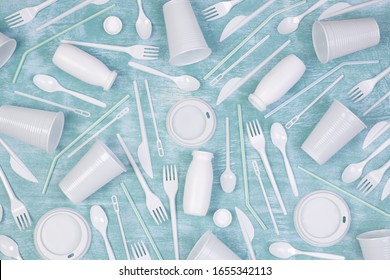 Disposable white single use plastic objects such as cups, forks, spoons and drinking straws on blue background