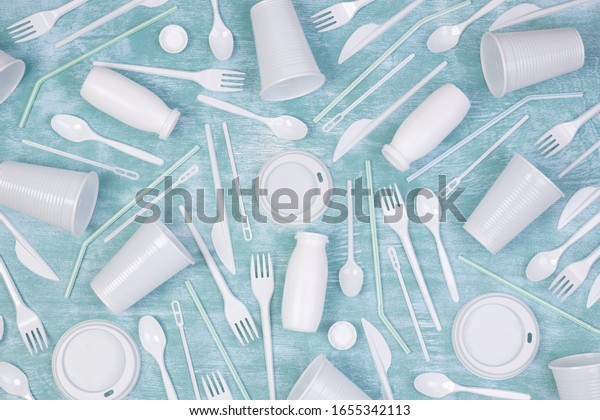 Disposable white\
single use plastic objects such as cups, forks, spoons and drinking\
straws on blue\
background