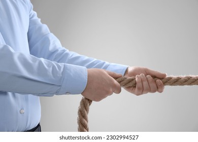 Dispute concept. Man pulling rope on light grey background, closeup - Powered by Shutterstock