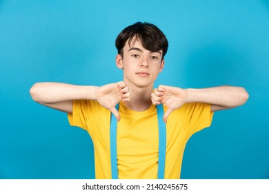 Dissapointed Teenager Boy With Thumbs Down Isolated On Blue Background