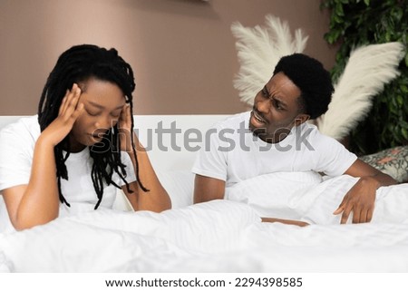 Dissatisfied angry unhappy African American dark skinned black couple sitting in bed in the morning arquing quarelling at home in the bedroom.