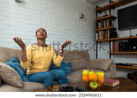 Dissatisfied annoyed stressed African American business woman sitting and working at home displeased cover ears with hands look up at ceiling suffer from noise from upstairs neighbors at home