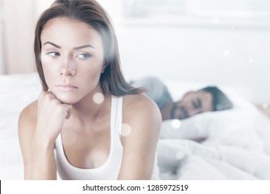 Dissatisfied Beautiful Young Woman In Bed With Sad Expression On Her Face, Sex Problems In Long Relationship Or Marriage While Man Sleeping. Saturation Or Satiety Between Caucasian Couple, Disinterest