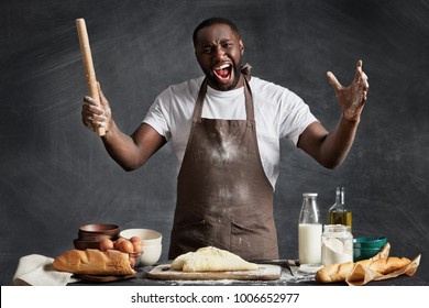 Dissatisfied black male cook dressed in kitchen uniform, holds rolling pin, gestures actively, being frustrated as can`t make good pastry, isolated over chalk black background. Unhappy chef. - Powered by Shutterstock