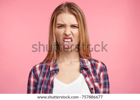 Dissatisfied female model frowns face, has disgusting expression, shows tongue, expresses non compliance, irritated with somebody, rejects do something. People and negative facial expressions