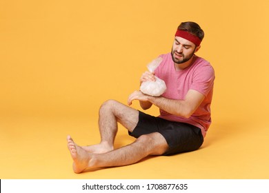 Dissatisfied Fitness Sporty Guy 20s Sportsman In Headband T-shirt In Home Gym Isolated On Yellow Background. Workout Sport Motivation Concept. Get Injured Hold Ice Pack Cooling Down Hand Wrist Pain