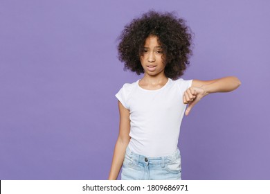 Dissatisfied Fun Little African American Kid Girl 12-13 Years Old In White T-shirt Isolated Showing Thumbs Down Dislike Gesture On Violet Wall Background Studio Portrait. Childhood Lifestyle Concept.