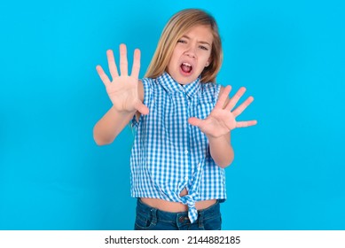 Dissatisfied Little Kid Girl With Glasses Wearing Plaid Shirt Over Blue Background Frowns Face, Has Disgusting Expression, Shows Tongue, Expresses Non Compliance, Irritated With Somebody.