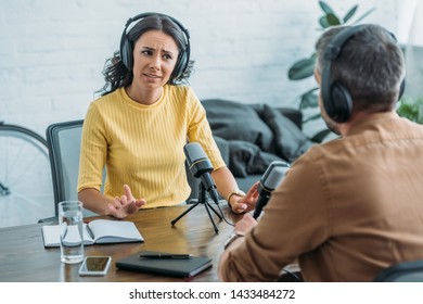 dissatisfied radio host gesturing while looking at colleague in broadcasting studio