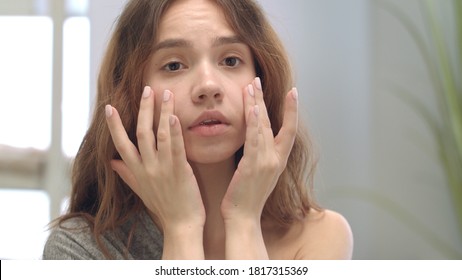 Dissatisfied Woman Touching Face Skin Front Bathroom Mirror. Young Woman Discontented Complexion Skin And Swelling Under Eyes. Problem Skin Care. Female Beauty