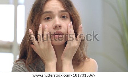 Dissatisfied woman touching face skin front bathroom mirror. Young woman discontented complexion skin and swelling under eyes. Problem skin care. Female beauty